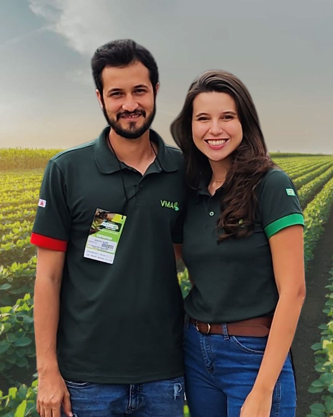Khiara Campos e o marido Bruno em pé lado a lado num campo de soja verde, sorrindo em uniforme de expositor.